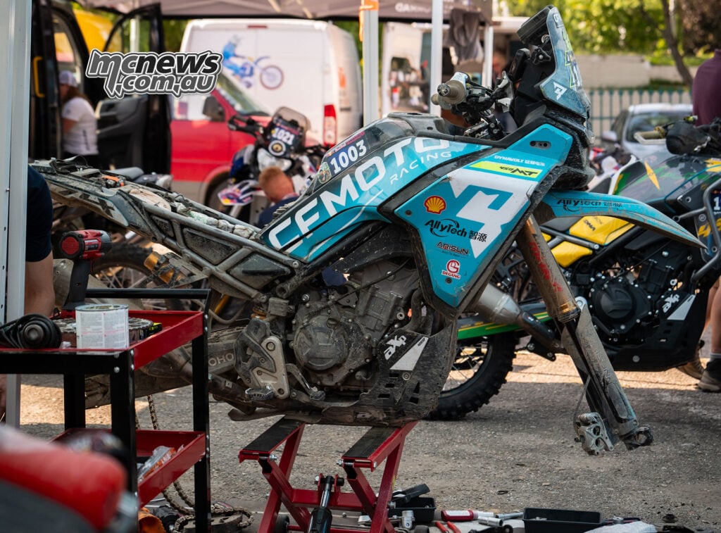 Dirty CFMOTO 450MT competition motorcycle on a paddock stand, partly dismantled for maintenance at Red Bull Romaniacs