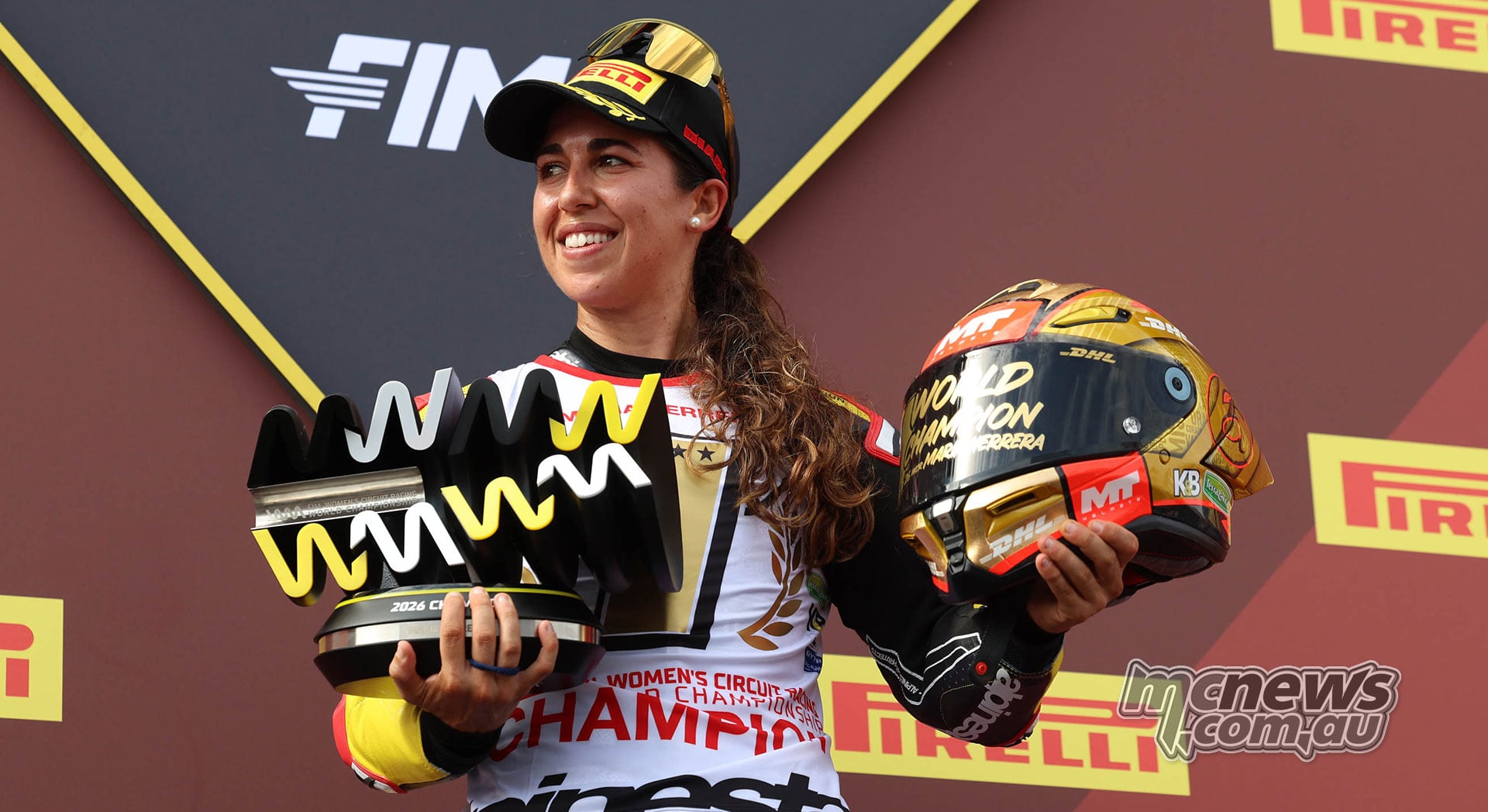 Maria Herrera smiles in her WorldWCR Champion shirt while holding the 2026 championship trophy and her gold helmet at Jerez