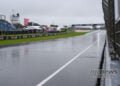 Rain-soaked Phillip Island main straight beside the pit wall, with empty blue grandstands under grey skies on Sunday morning