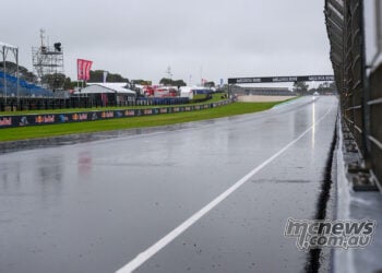 Rain-soaked Phillip Island main straight beside the pit wall, with empty blue grandstands under grey skies on Sunday morning
