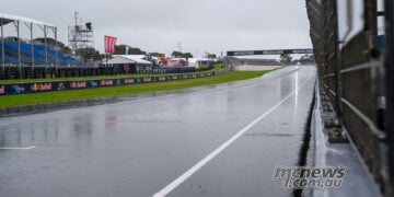Rain-soaked Phillip Island main straight beside the pit wall, with empty blue grandstands under grey skies on Sunday morning