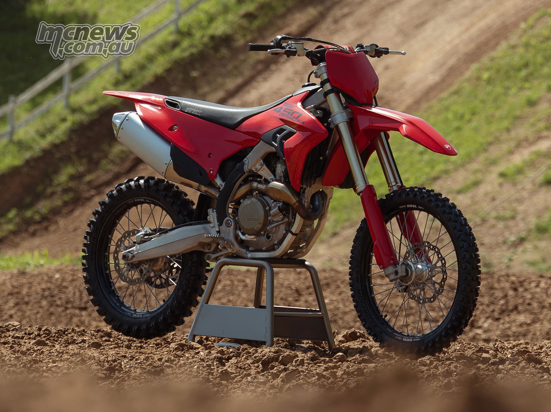 Front three-quarter view of the red 2027 Ducati Desmo450 MX on a motocross stand, showing its silver exhaust, gold Showa forks and black Ducati graphics.