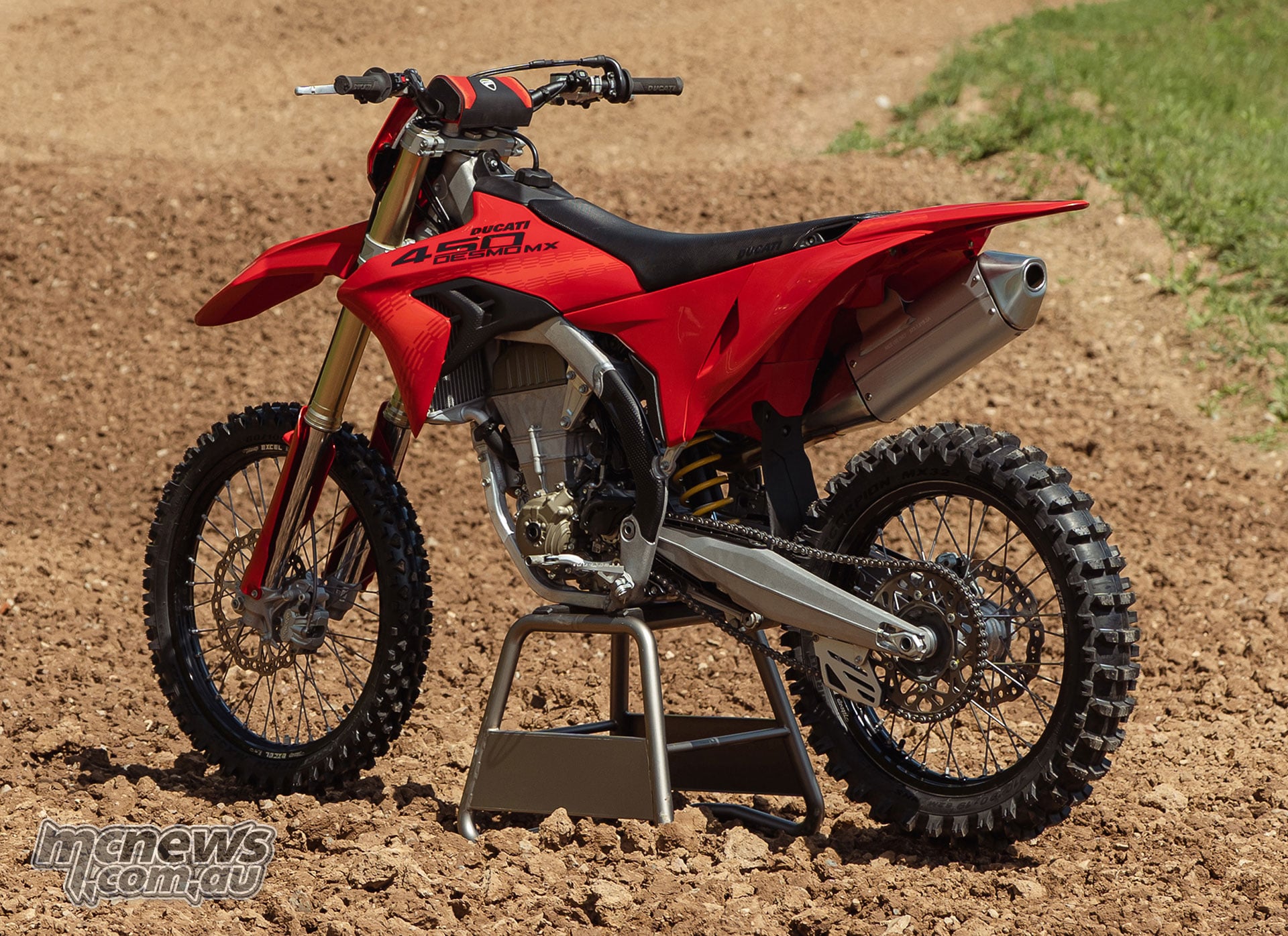 Rear three-quarter view of the 2027 Ducati Desmo450 MX showing the rear sprocket, drive chain, aluminium swingarm, knobbly tyres and silver silencer.
