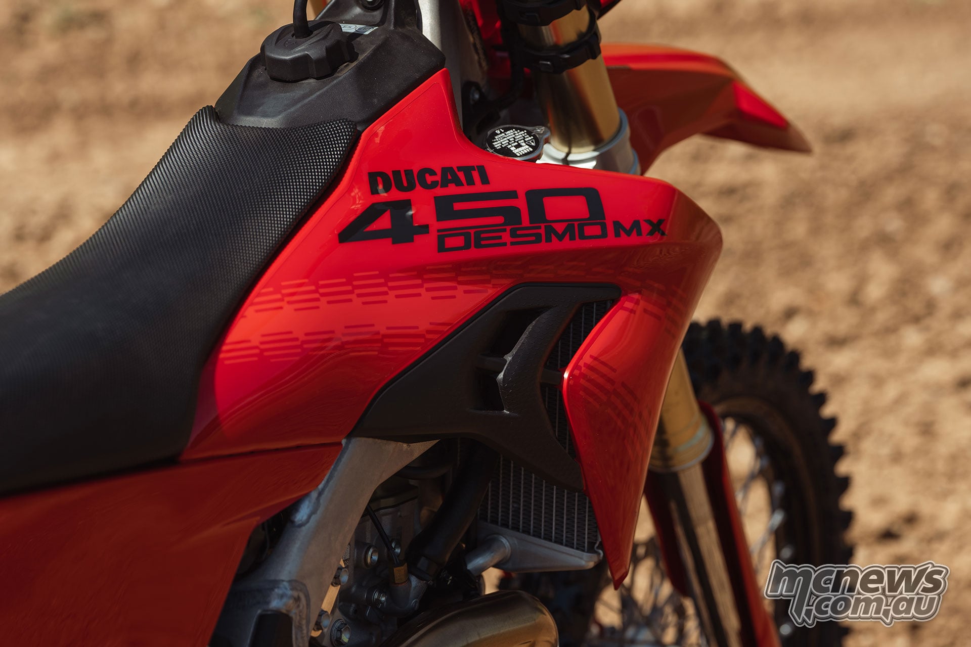 Close-up of the 2027 Ducati Desmo450 MX red fuel-tank shroud with black 450 Desmo MX graphics, textured seat and fuel filler cap.