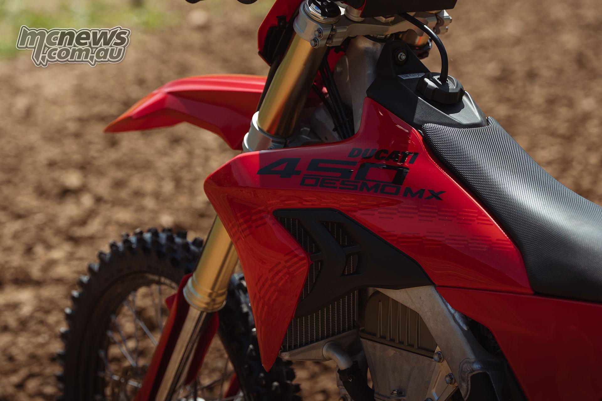 Detailed side view of the 2027 Ducati Desmo450 MX red radiator shroud showing its black Ducati and 450 Desmo MX logos beside the seat and gold front fork.