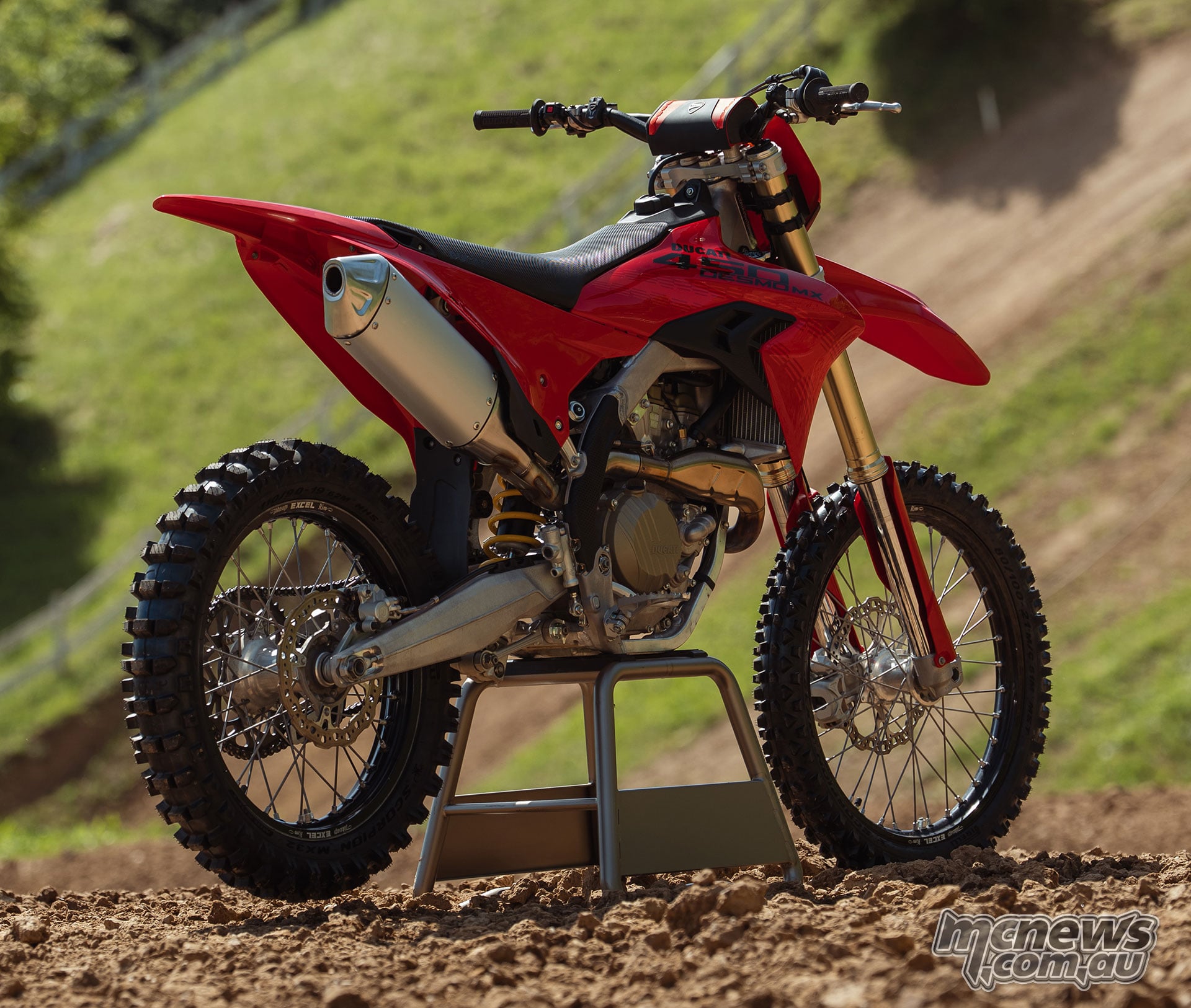 Rear three-quarter view of the red 2027 Ducati Desmo450 MX on a stand, showing its silver exhaust silencer, rear wheel, aluminium swingarm and exposed engine.