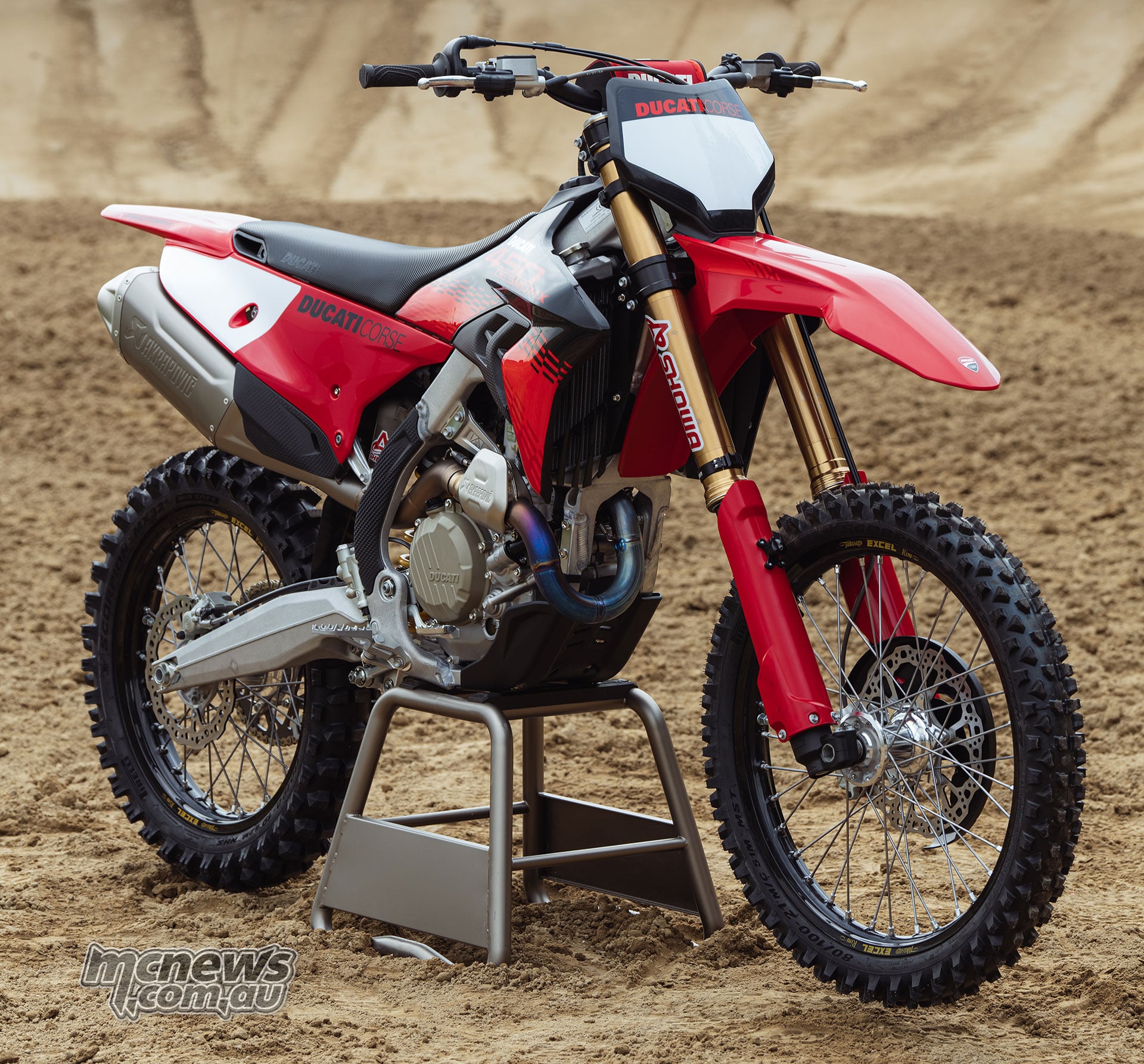 Front three-quarter view of the 2027 Ducati Desmo450 MX Factory showing its red, black and white Ducati Corse livery, Akrapovic titanium exhaust header and Showa suspension.