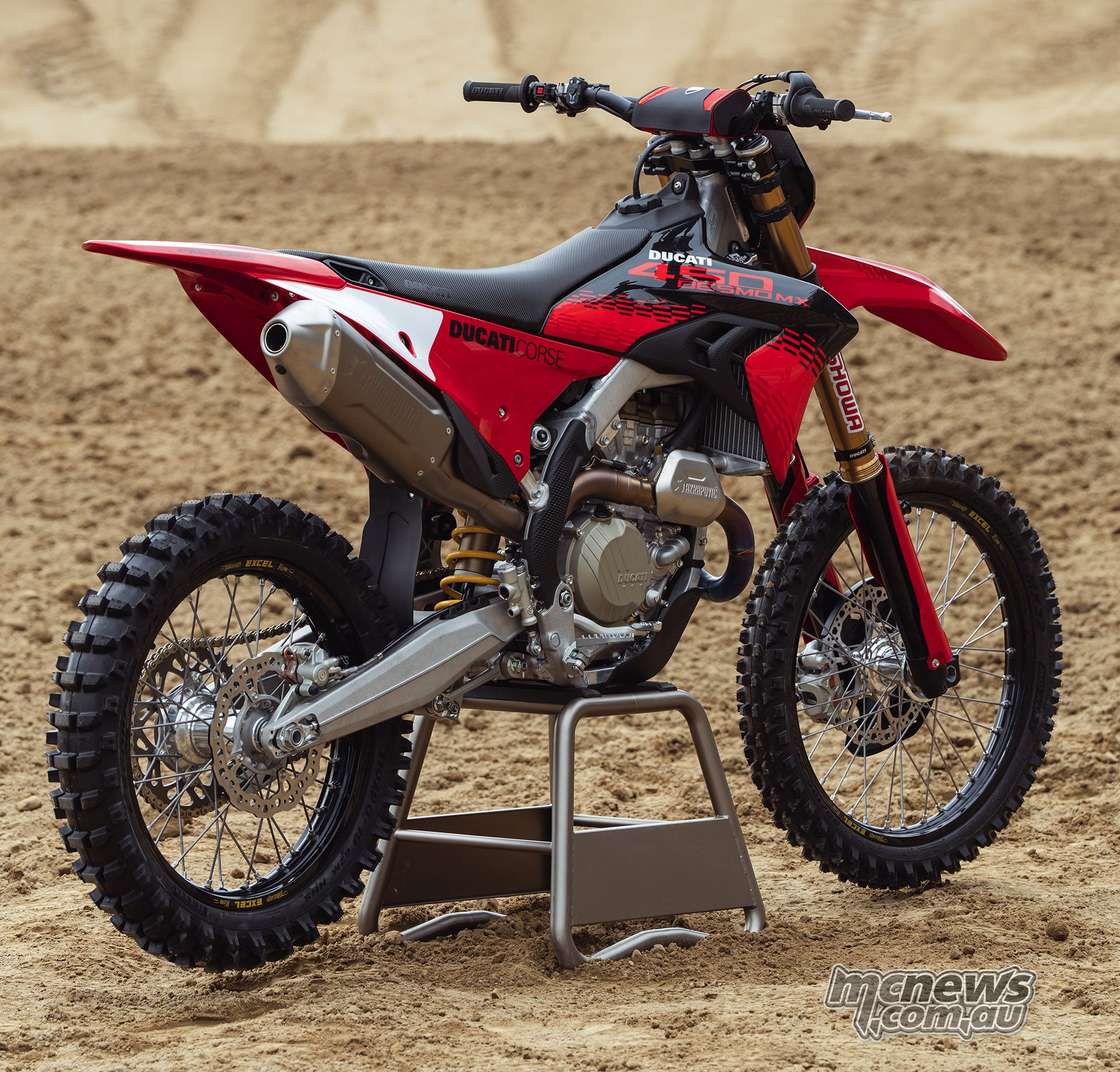 Rear three-quarter view of the 2027 Ducati Desmo450 MX Factory showing its Akrapovic titanium silencer, Ducati Corse bodywork, gold Showa forks and aluminium chassis.