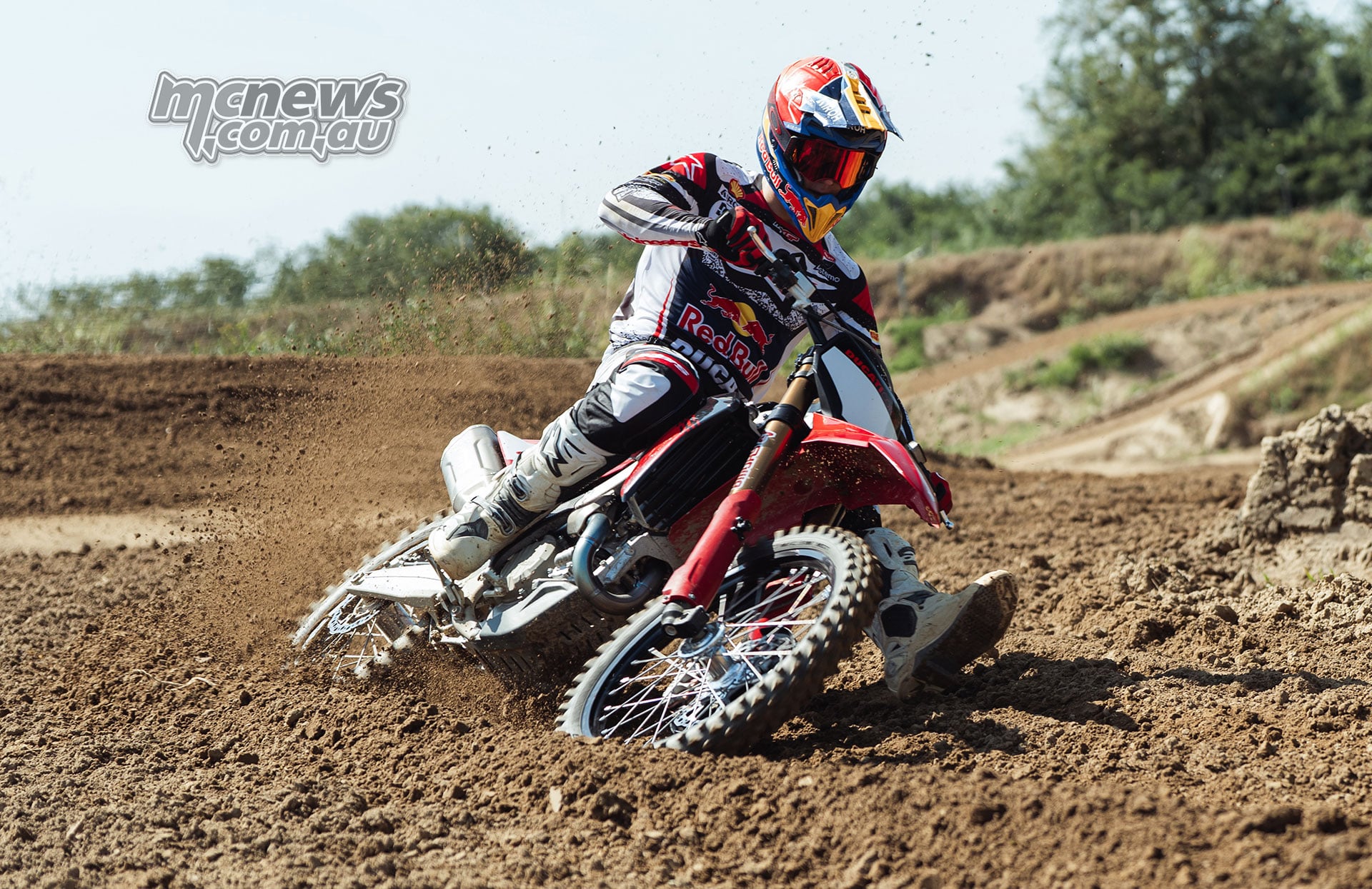 Motocross rider in Red Bull racing gear leaning a Ducati Desmo450 MX Factory into a dirt-track corner with the front wheel carving through a rut and dirt spraying behind.