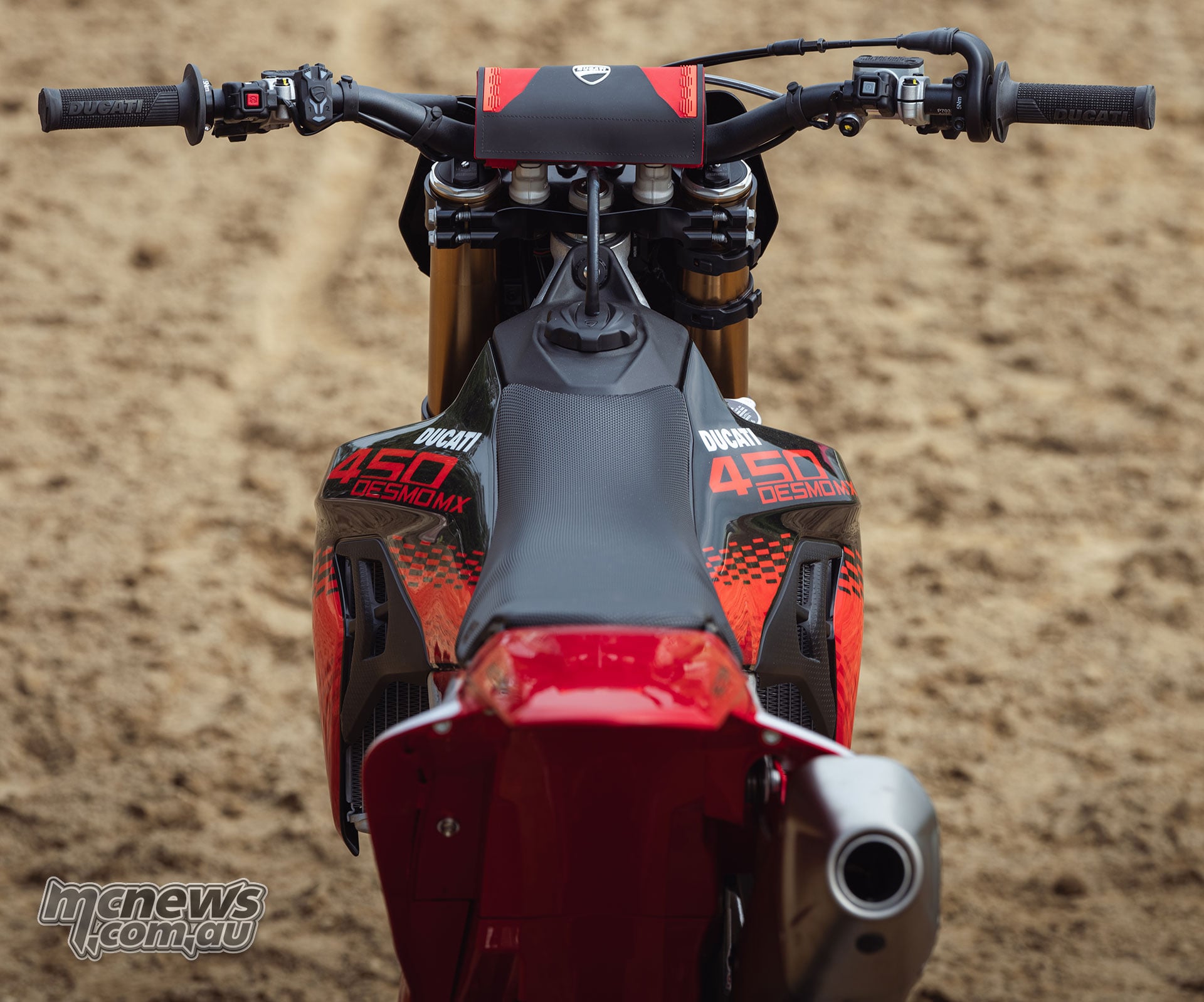 Overhead view along the seat of the 2027 Ducati Desmo450 MX Factory towards its handlebars, fuel cap, steering head, controls and red and black Ducati graphics.