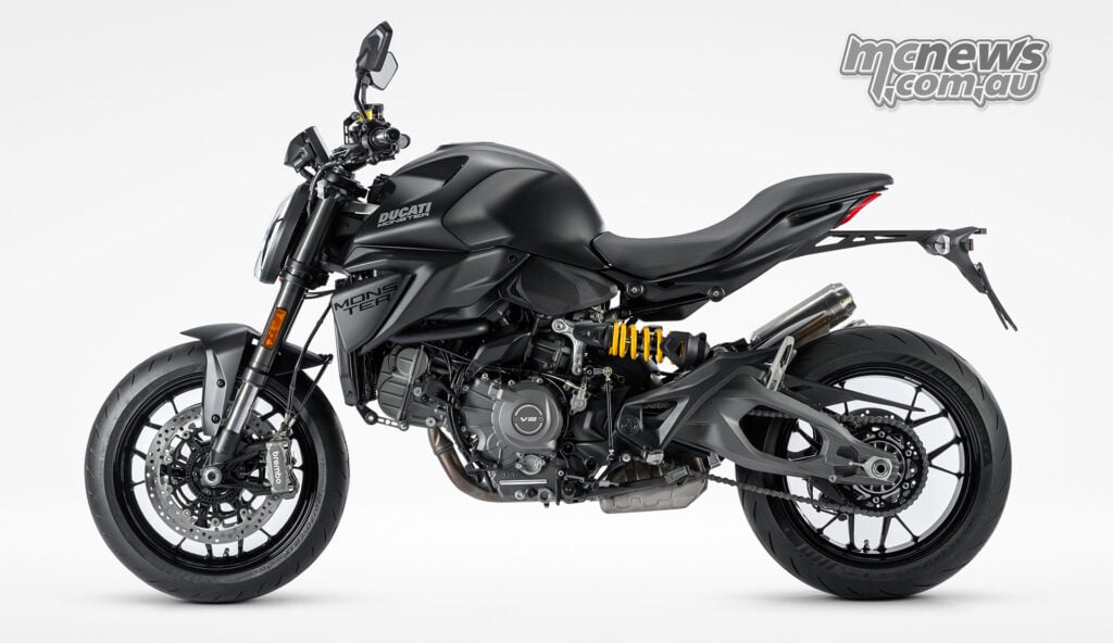 Full left-side profile of the 2027 Ducati Monster Dark, showing the V2 engine, yellow shock spring and chain drive