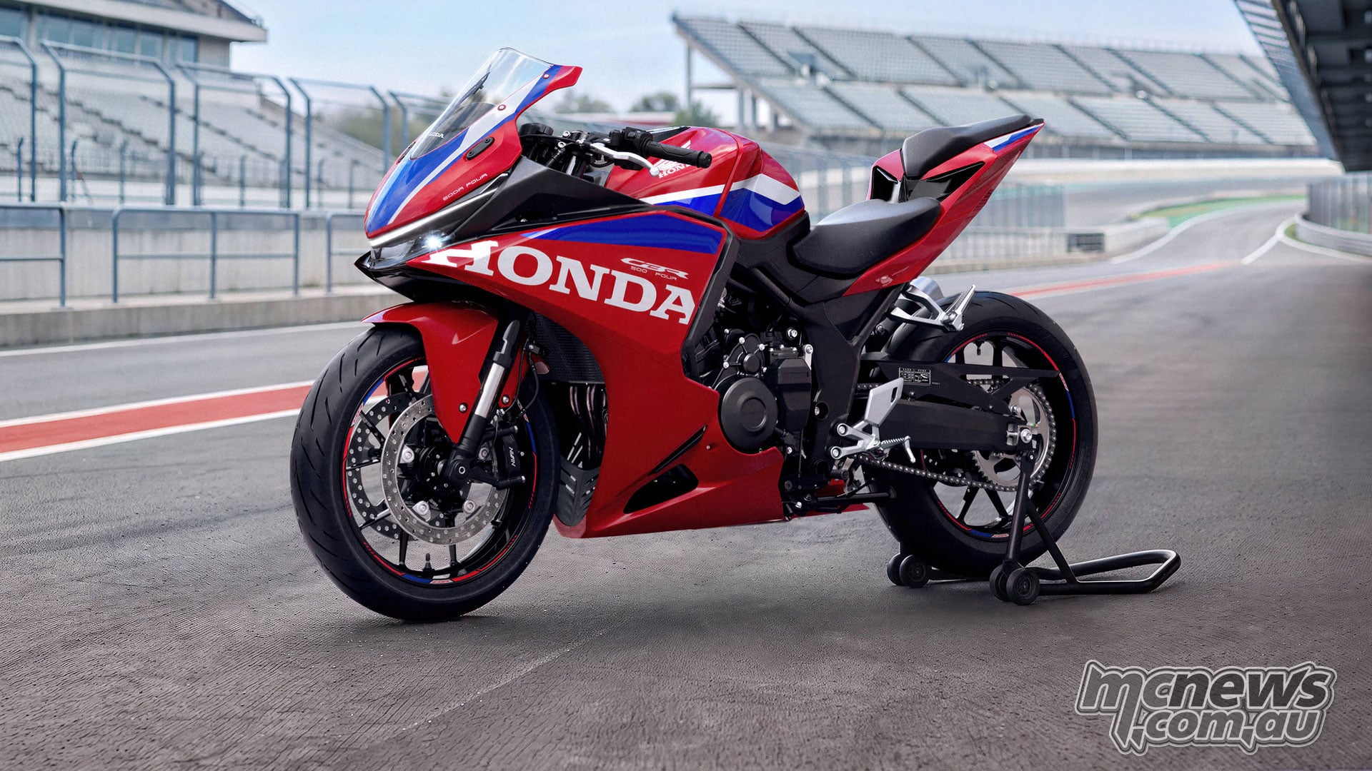 Red 2027 Honda CBR500R FOUR on a rear paddock stand in pit lane, viewed from the front left