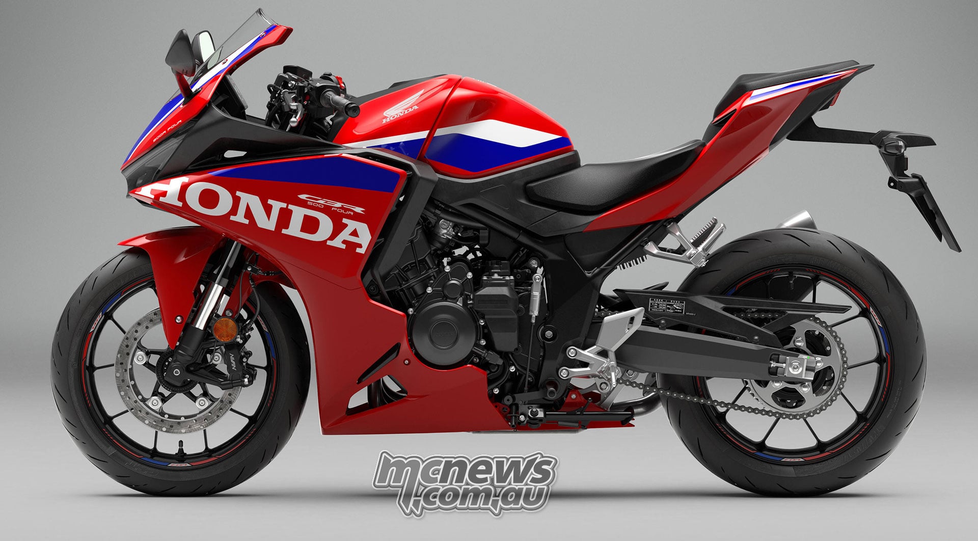 Full left-side studio profile of the red 2027 Honda CBR500R FOUR showing its engine, chain drive and aluminium swingarm