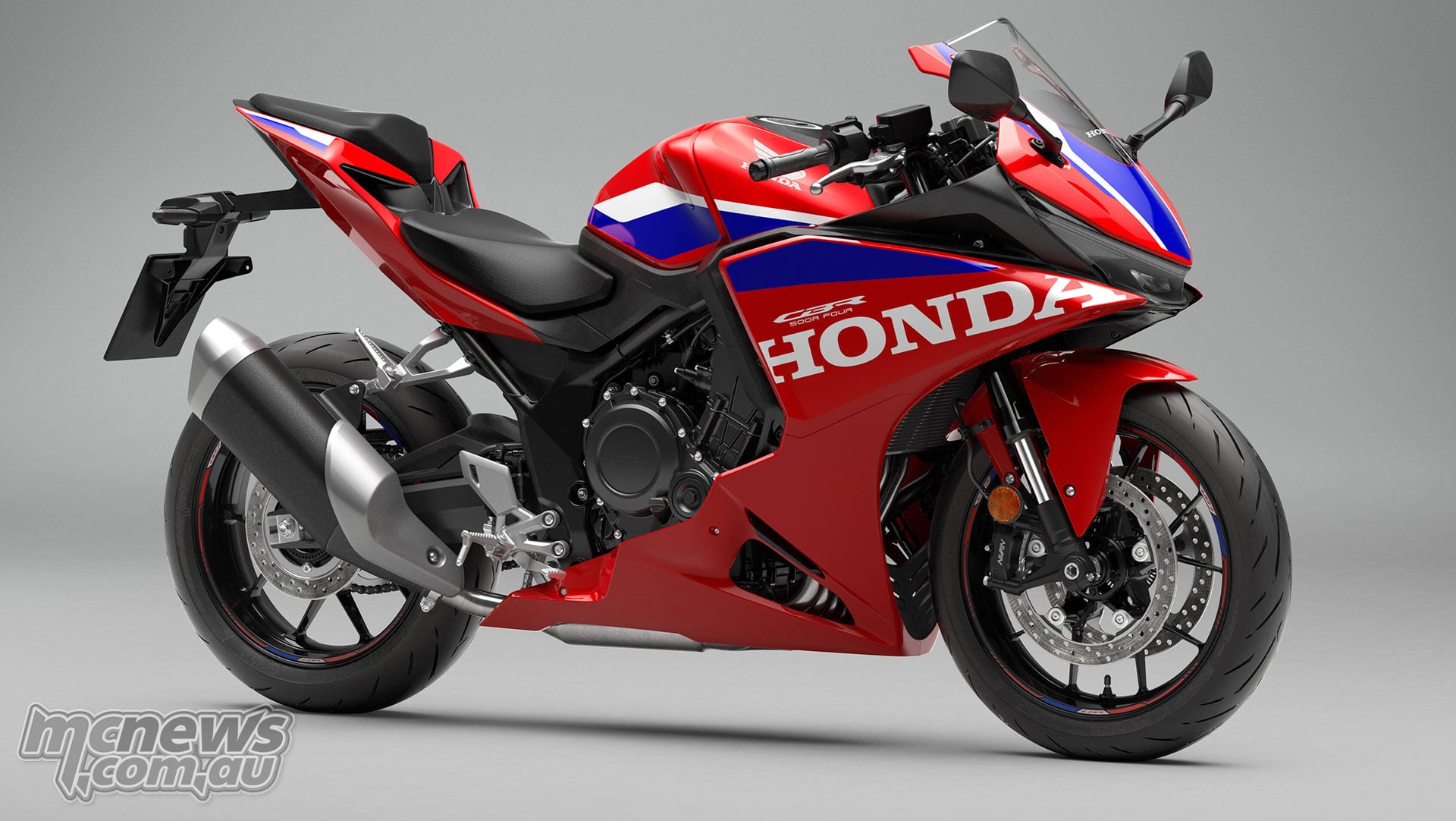 Full front right three-quarter studio view of the red 2027 Honda CBR500R FOUR showing the front brake and exhaust