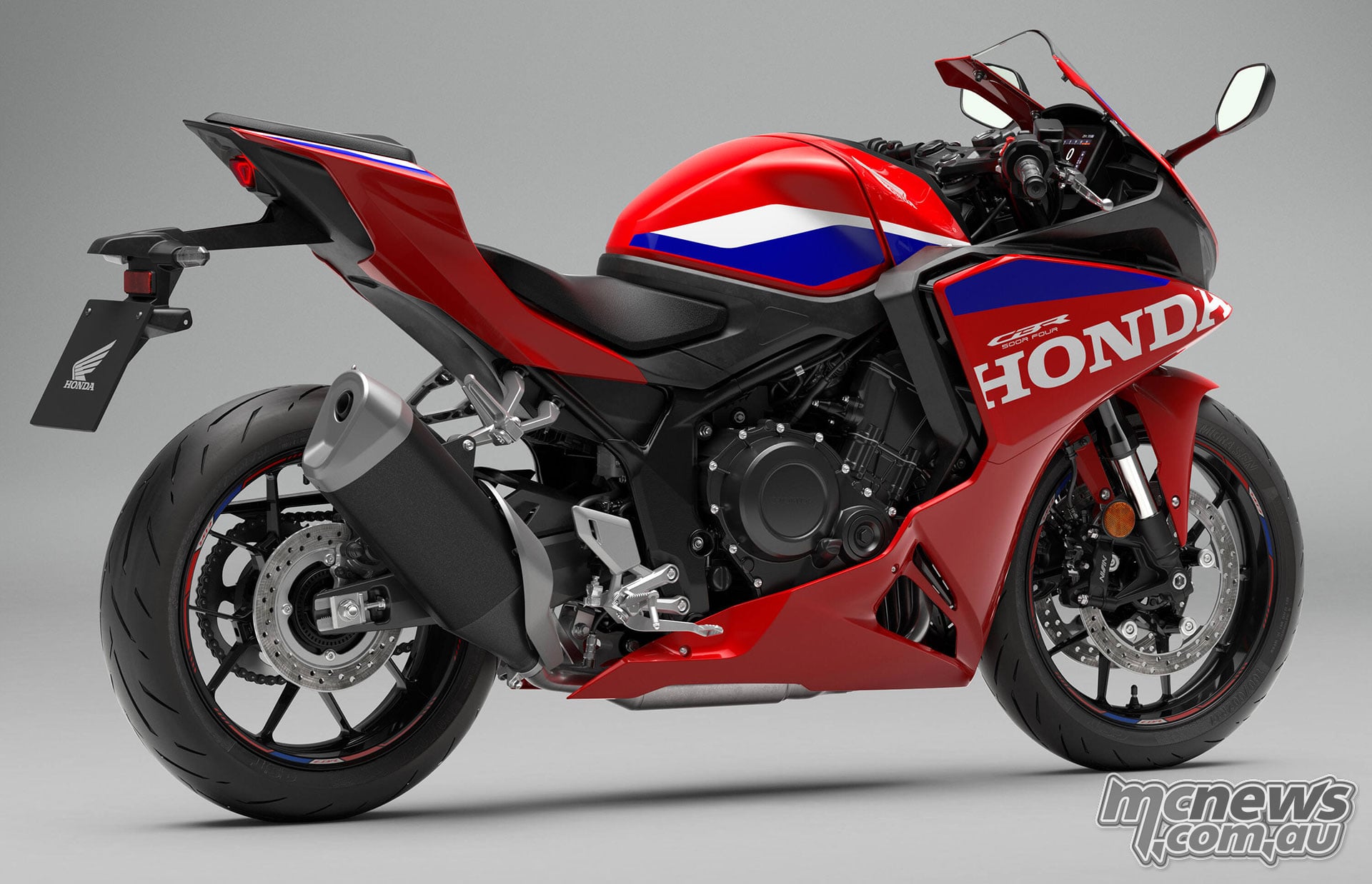 Rear right three-quarter studio view of the red 2027 Honda CBR500R FOUR showing the exhaust, engine and stepped seats