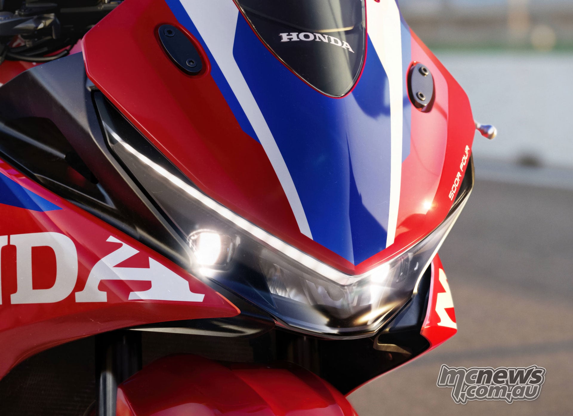 Illuminated headlights and daytime-running lights on the red 2027 Honda CBR500R FOUR with its mirrors removed