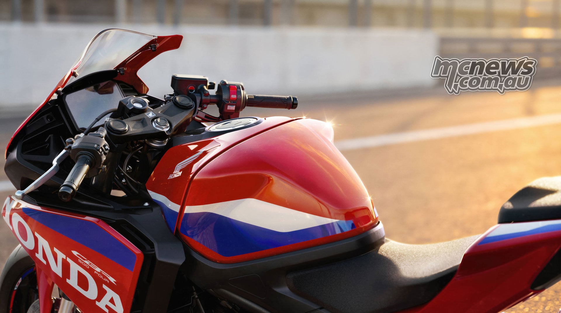 Close-up of the red 2027 Honda CBR500R FOUR fuel tank, rider seat and handlebars in warm sunlight