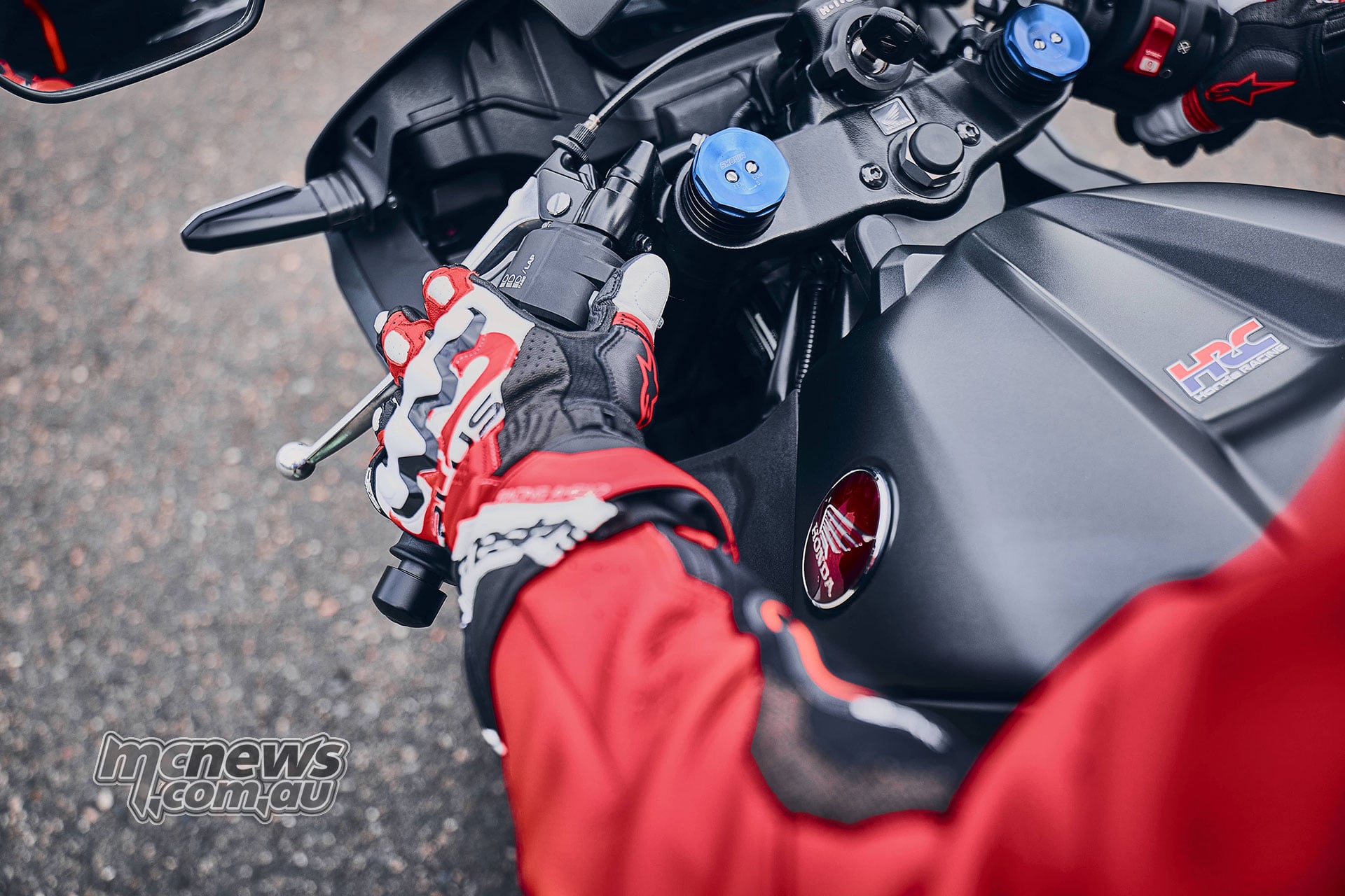Gloved rider operating the left handlebar controls of the black 2027 Honda CBR600RR, viewed above the fuel tank
