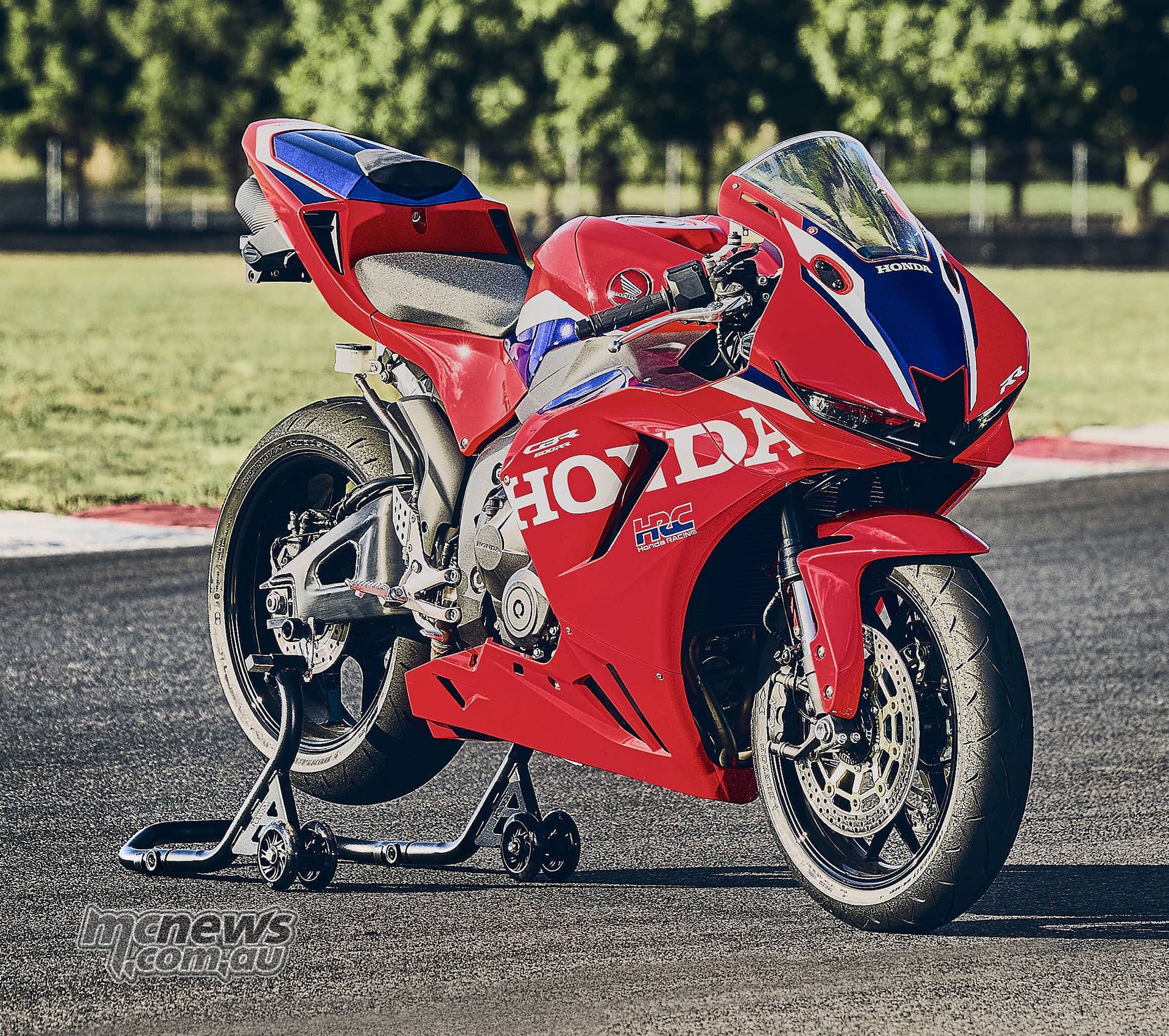 Red 2027 Honda CBR600RR on a rear paddock stand outdoors, viewed from the front right