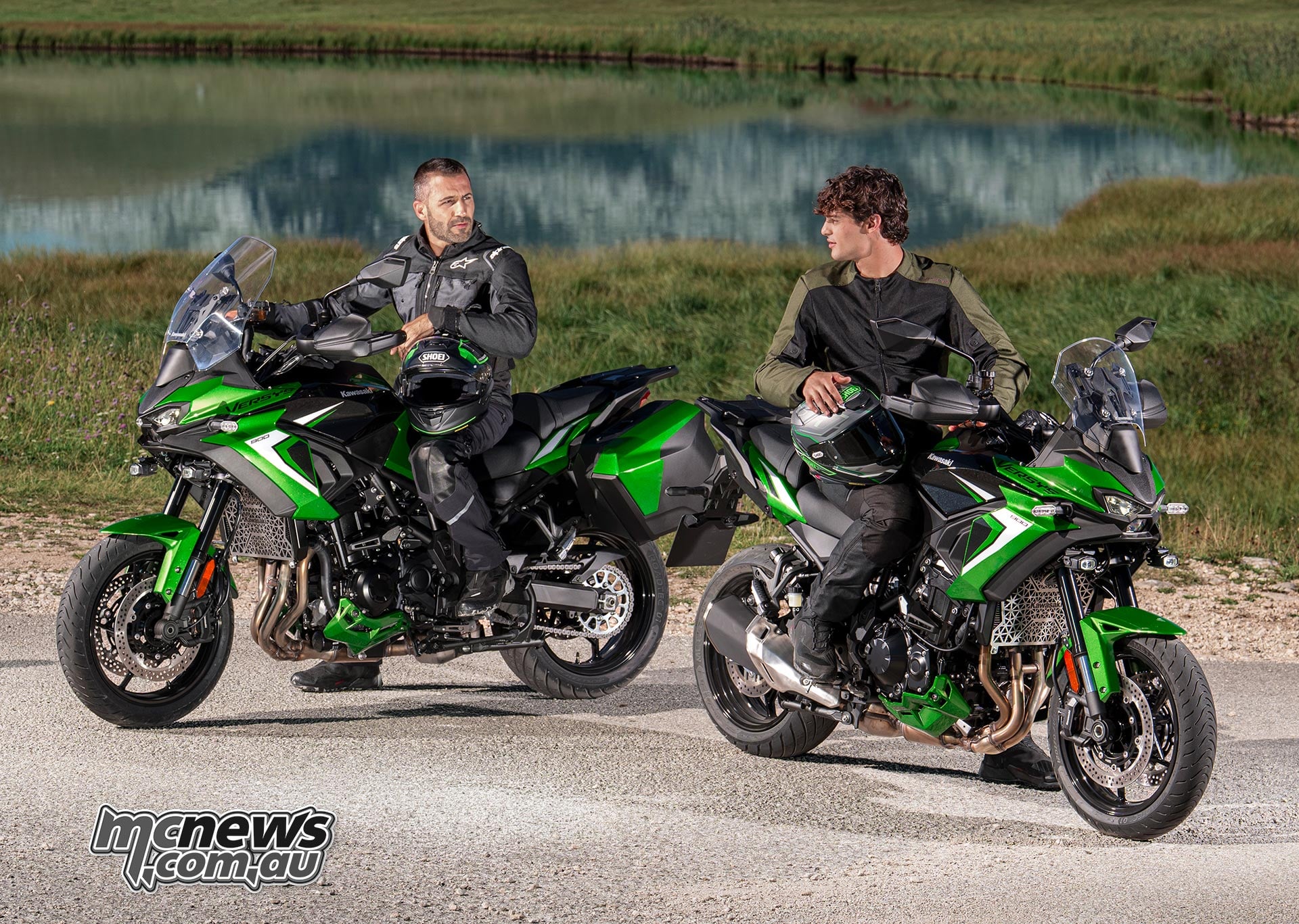 Two riders sitting on green Kawasaki Versys 900 SE motorcycles parked beside a lake