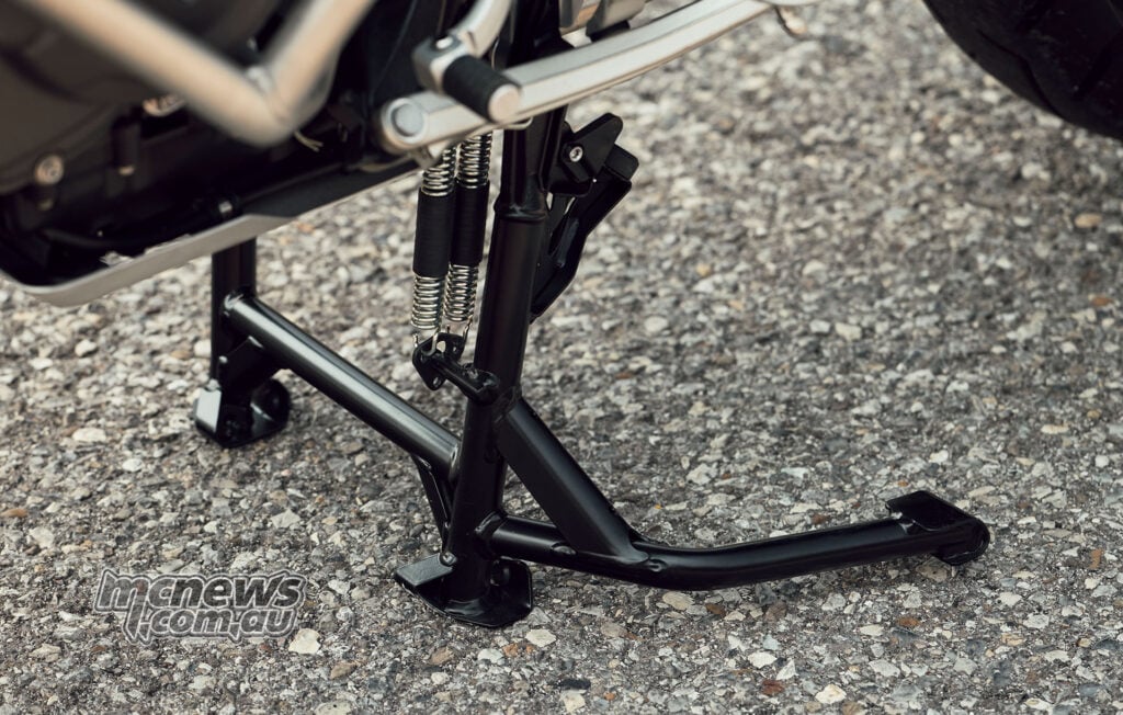 Close-up of the deployed centre stand and its return springs on a 2027 Triumph Tiger 1200 GT Explorer.