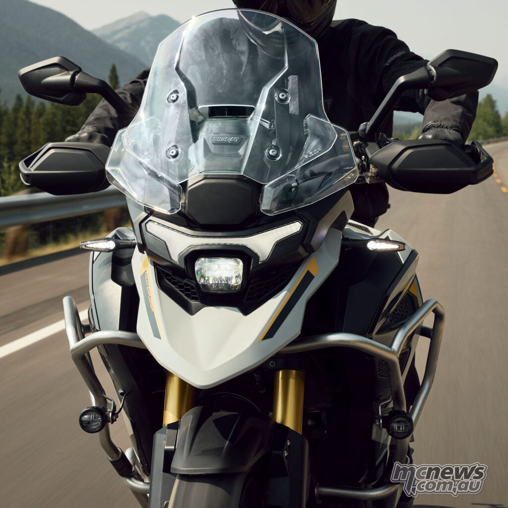 Front view of a rider on a 2027 Triumph Tiger 1200 Rally Explorer, showing its windscreen and illuminated headlight.