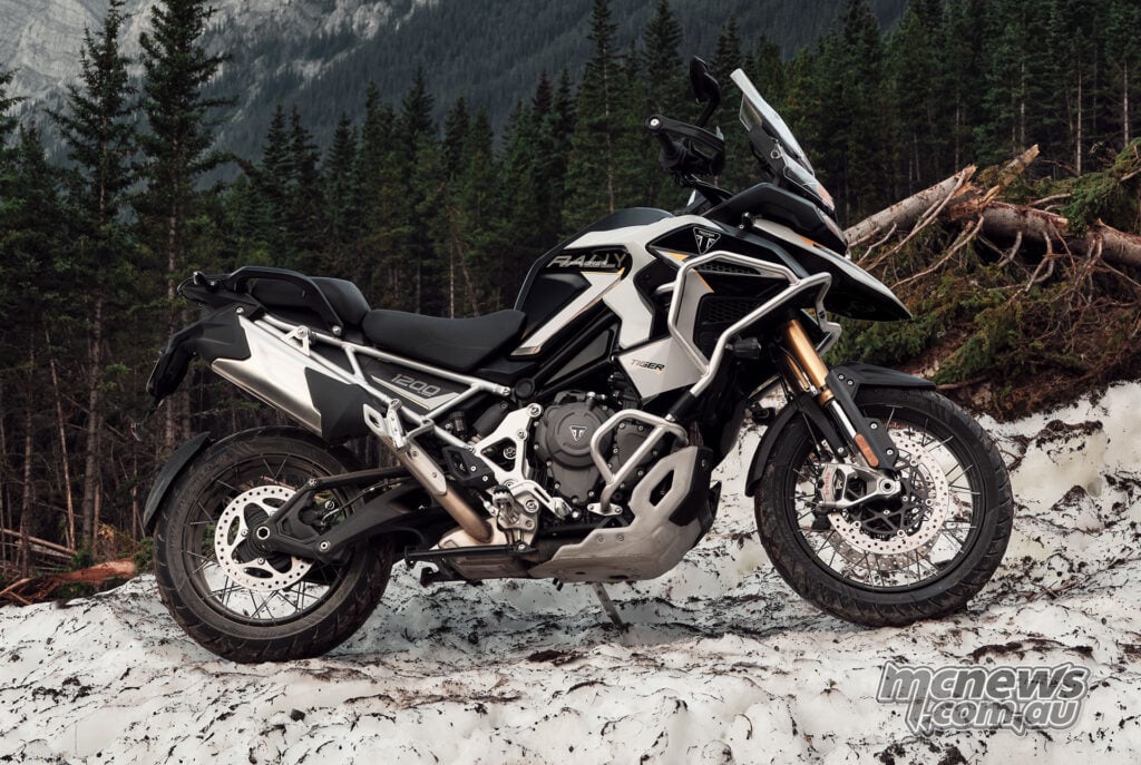 A 2027 Triumph Tiger 1200 Rally Explorer parked on snow beside a forest, viewed from its right side.