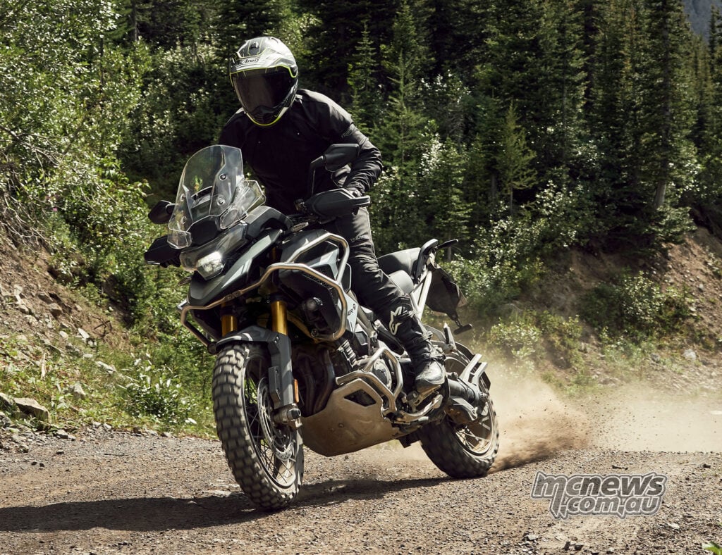 A rider stands on an accessory-equipped 2027 Triumph Tiger 1200 Rally Pro while riding a dusty track.