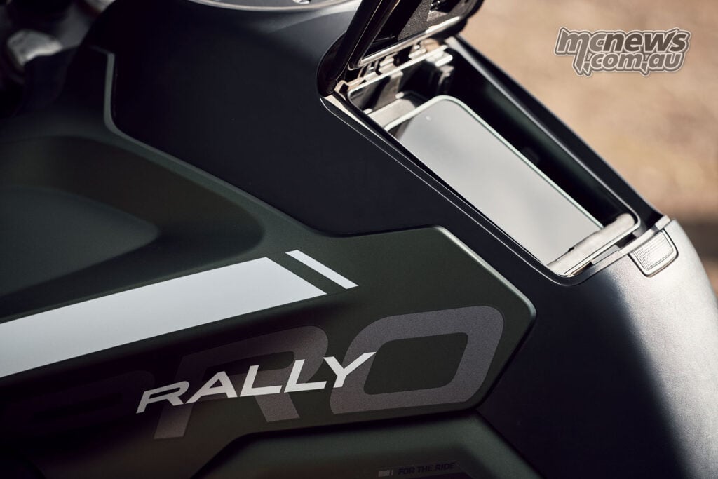 A smartphone sits inside the open tank-top storage compartment on a green 2027 Triumph Tiger 1200 Rally Pro.