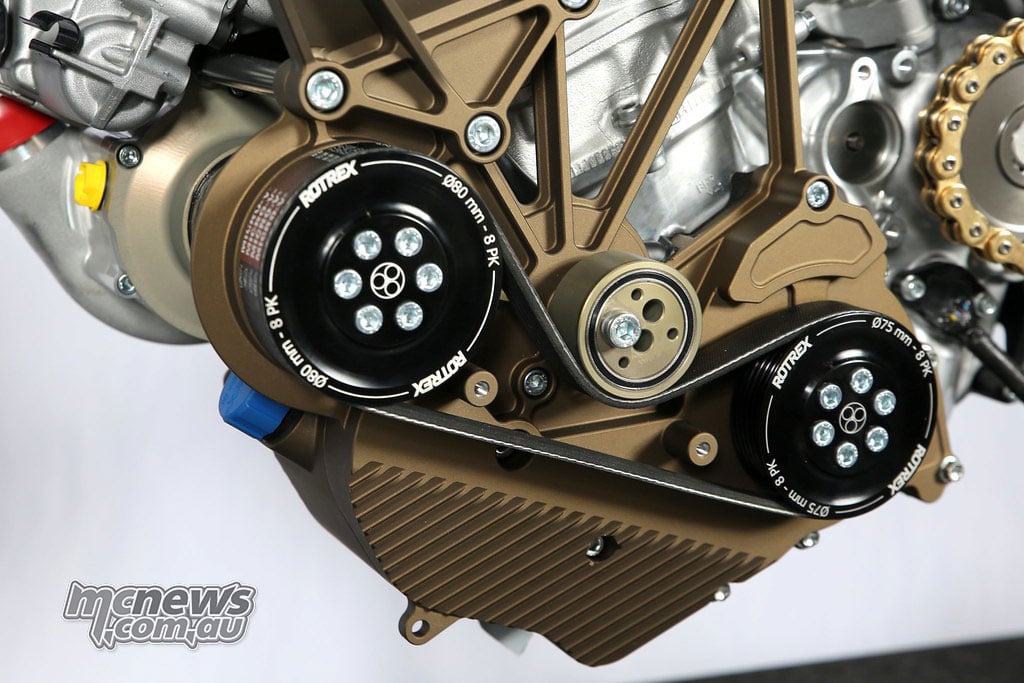 Exposed supercharger drive belt and pulleys on a gold-coloured machined mounting assembly.