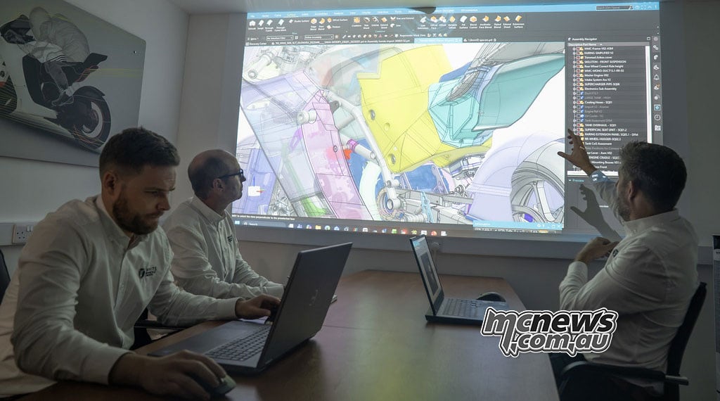Three WMC engineers discussing a projected CAD model of the Mono RR powertrain.