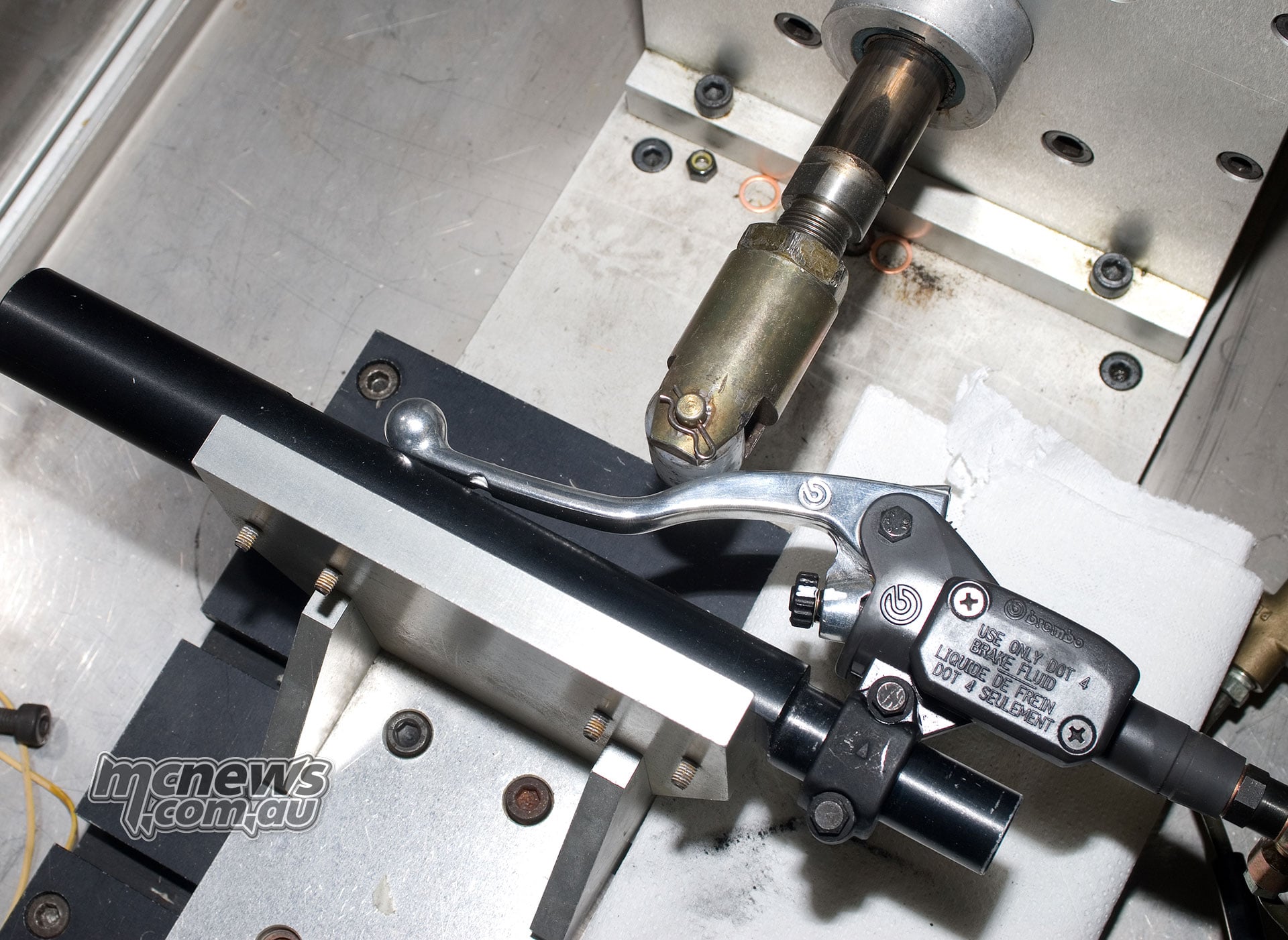 Actuator touching a Brembo brake lever beside its master cylinder and fluid reservoir on a metal test fixture.
