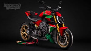 Three-quarter front studio view of Ducati Diavel V4 RS 100 with red and green bodywork, gold wheels and black exhaust system.