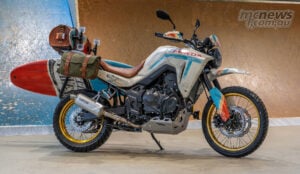 Side view of Honda XL750 Transalp Ocean Nomad custom with surfboard, leather seat and gold wheels