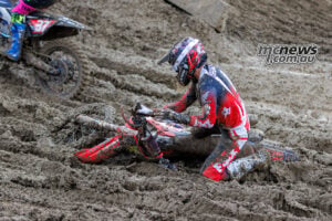 Jo Shimoda kneels beside his fallen Honda in deep mud as Cole Davies' number 37 Yamaha passes at the upper left.