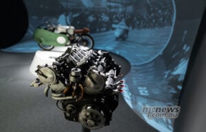 Eight cylinders, eight carburettors and just 500cc: the V8’s compact engine helps explain both its brilliance and its complexity. Exposed Moto Guzzi V8 engine with intake trumpets and exhaust pipes, with the green racing motorcycle behind.